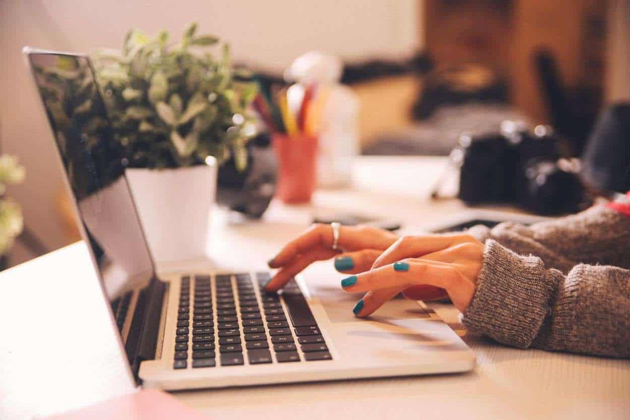 A woman's hands at a laptop with seasonal foliage in the background